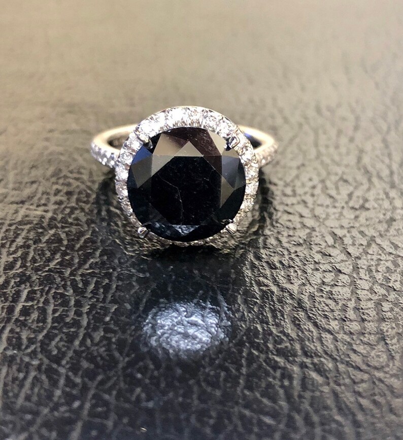 May include: A black diamond engagement ring with a halo of smaller diamonds set in a white gold band.