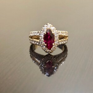 May include: A gold ring with a marquise-shaped ruby surrounded by a halo of small diamonds. The ring has a delicate band with additional diamonds.