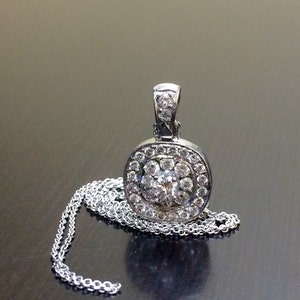 May include: A silver pendant necklace with a round, oval-shaped pendant featuring a cluster of small diamonds surrounding a larger center diamond.
