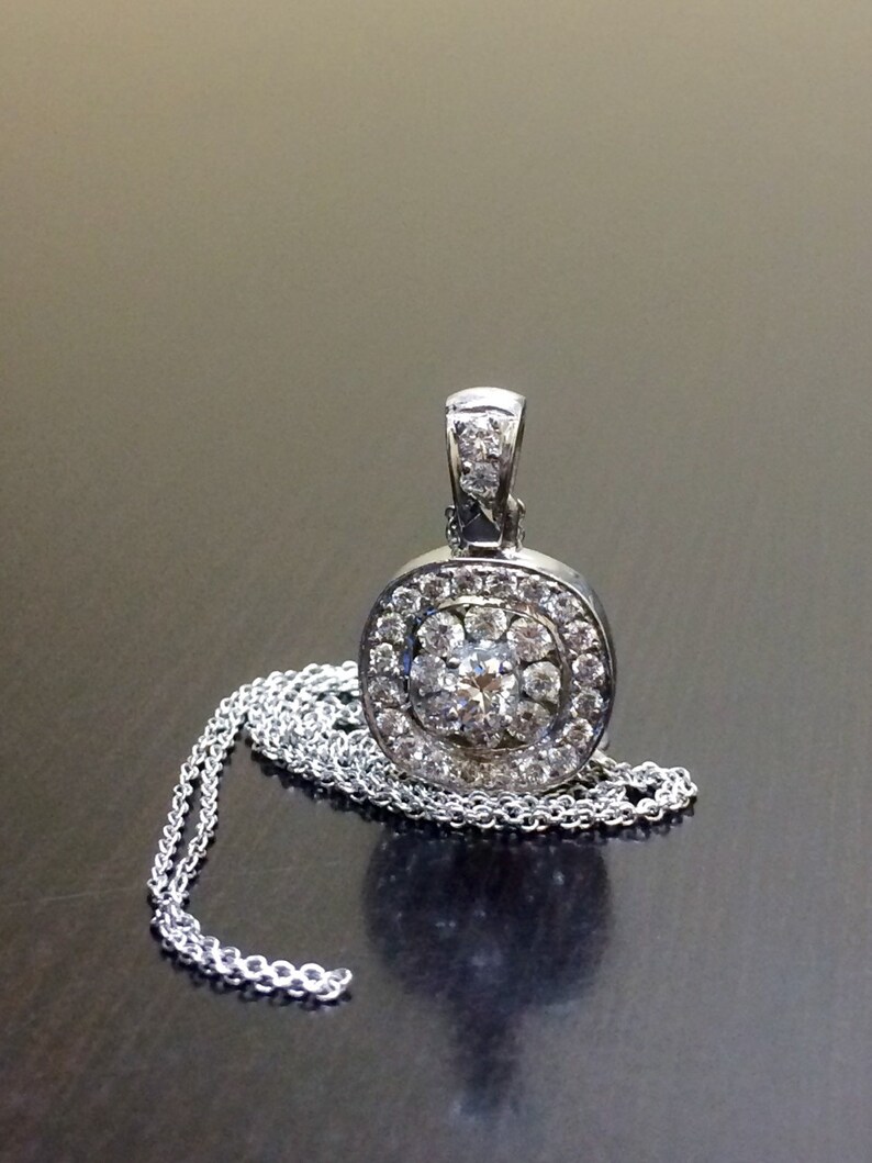 May include: A silver pendant necklace with a round, oval-shaped pendant featuring a cluster of small diamonds surrounding a larger center diamond.