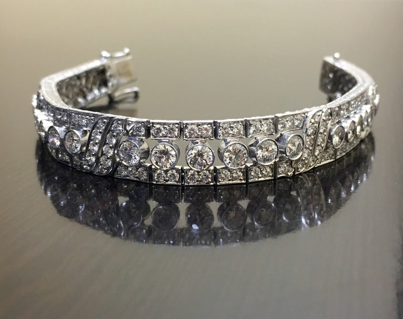 Puede incluir: Un brazalete de plata con una fila de diamantes redondos grandes engastados en pav&eacute;. El brazalete est&aacute; hecho de metal y tiene un acabado pulido.
