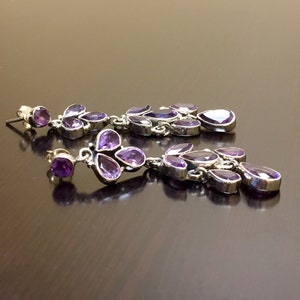 May include: A pair of long, dangling earrings with multiple purple amethyst stones set in silver.