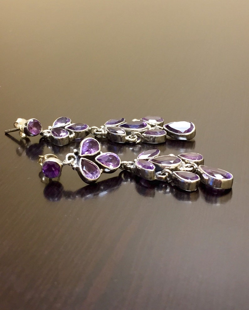 May include: A pair of long, dangling earrings with multiple purple amethyst stones set in silver.