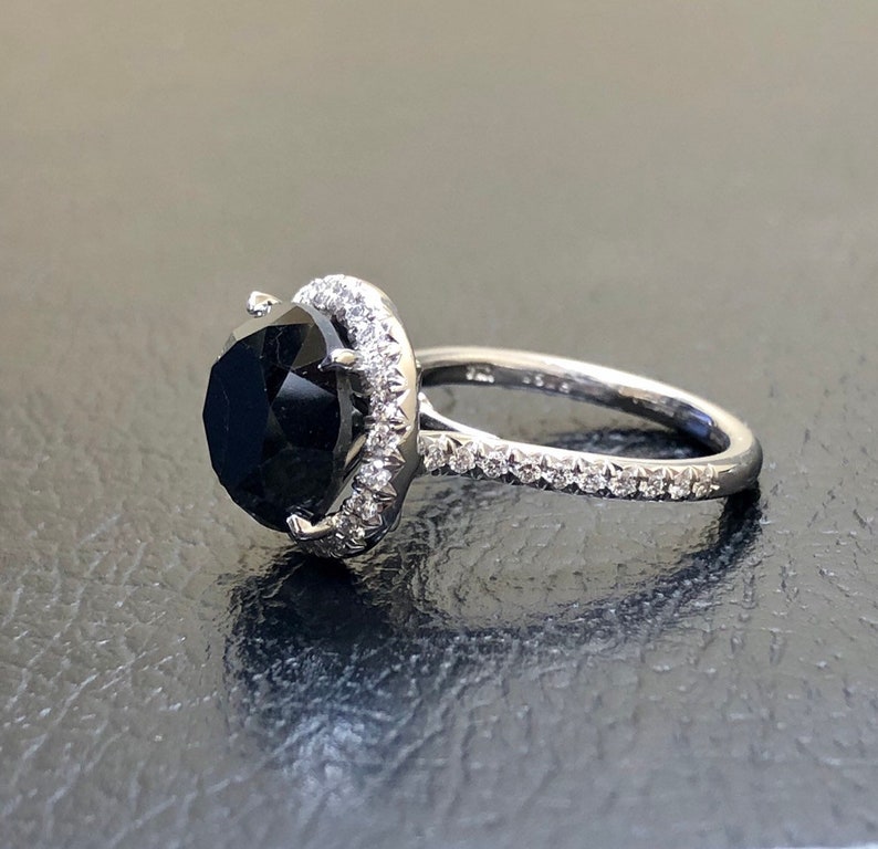 May include: A black diamond engagement ring with a halo of smaller diamonds set in white gold.