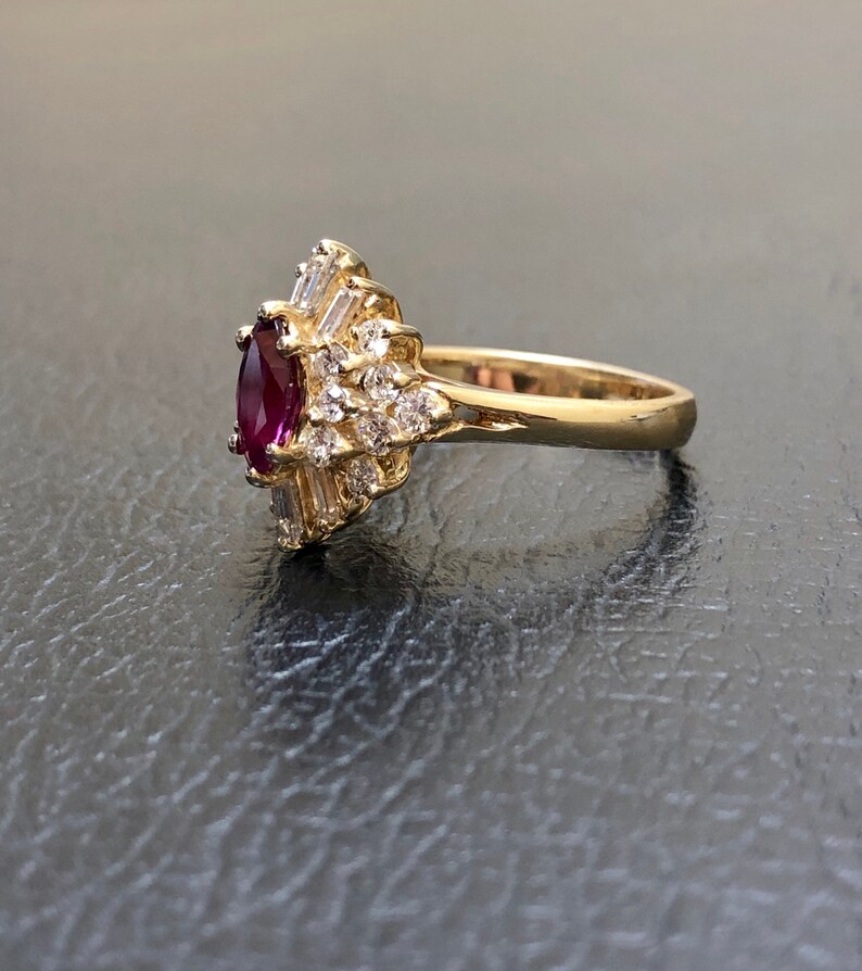 Op de afbeelding: Een gouden ring met een grote, ovale robijn omringd door kleinere, heldere diamanten.