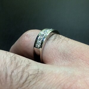 K&ouml;nnte beinhalten: Ein silberner Ring mit einer Reihe kleiner, klarer Diamanten, die in einer Kanalfassung gefasst sind.