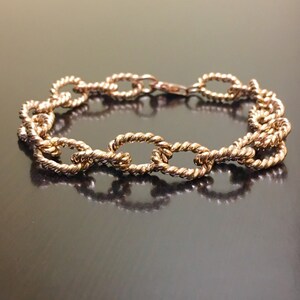 Puede incluir: Un brazalete dorado con un dise&ntilde;o de cadena tipo cuerda. El brazalete est&aacute; hecho de eslabones ovalados.