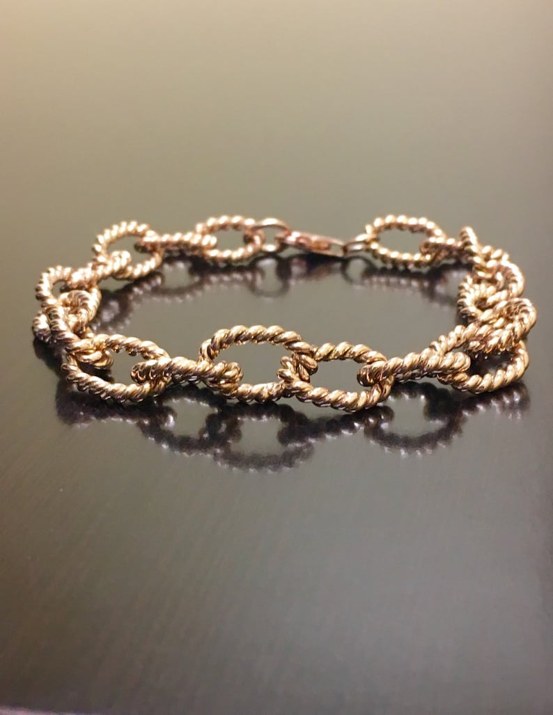 Puede incluir: Un brazalete dorado con un dise&ntilde;o de cadena tipo cuerda. El brazalete est&aacute; hecho de eslabones ovalados.