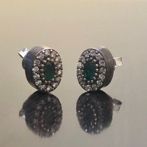 May include: A pair of silver earrings with a green oval gemstone surrounded by smaller white gemstones.