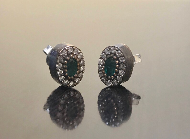 May include: A pair of silver earrings with a green oval gemstone surrounded by smaller white gemstones.