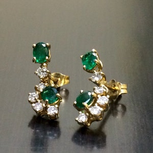 May include: A pair of gold earrings with emerald and diamond accents. The earrings feature a cluster of small diamonds surrounding a larger emerald gemstone.