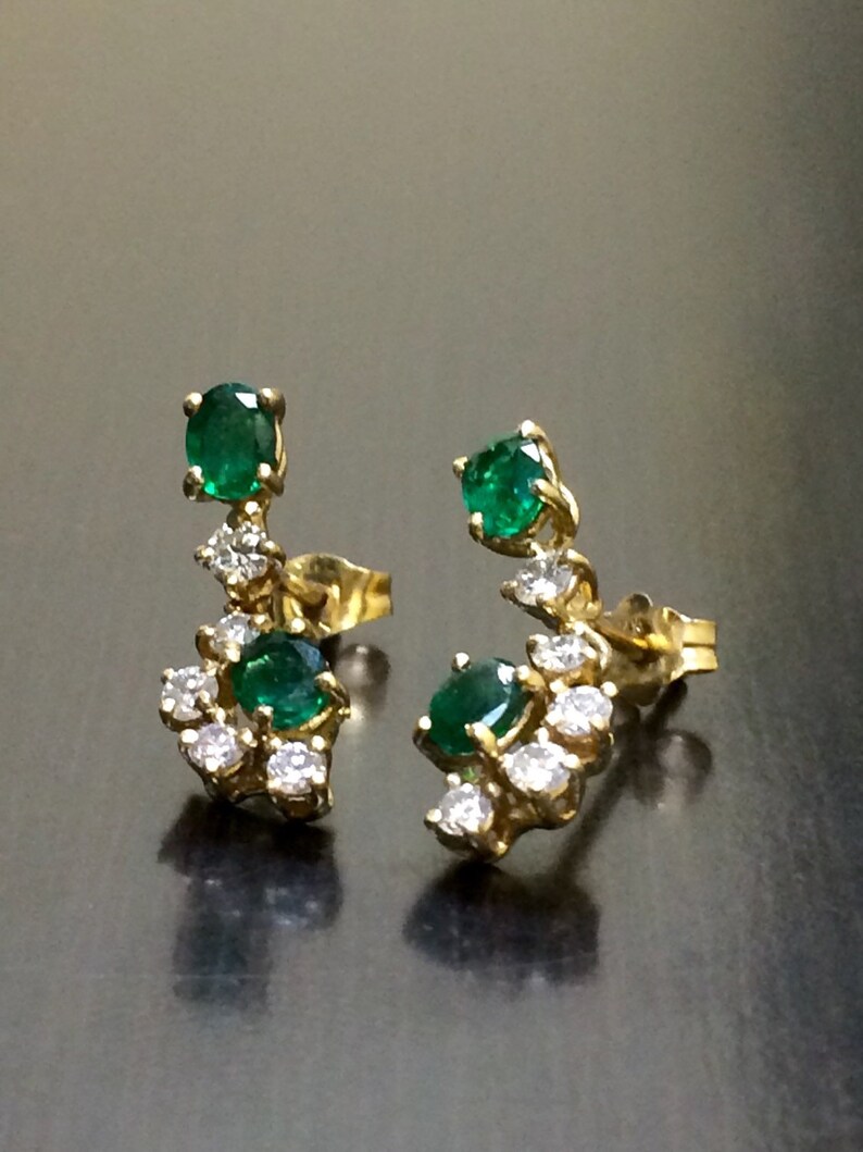 May include: A pair of gold earrings with emerald and diamond accents. The earrings feature a cluster of small diamonds surrounding a larger emerald gemstone.