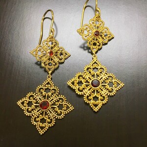 May include: Gold filigree earrings with red gemstone accents. The earrings feature a delicate, intricate design with multiple layers of filigree.