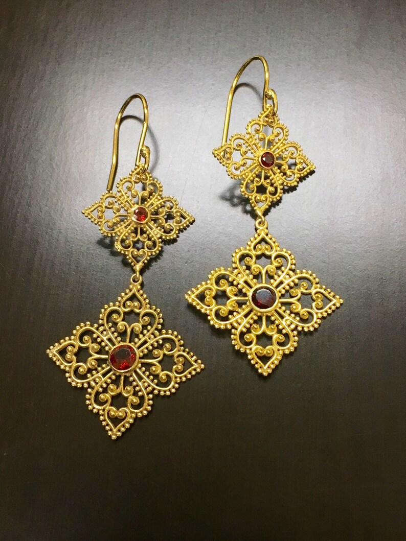 May include: Gold filigree earrings with red gemstone accents. The earrings feature a delicate, intricate design with multiple layers of filigree.