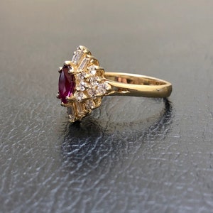 May include: A gold ring featuring a large, oval ruby surrounded by smaller diamonds. The ring is set in a delicate, floral design.