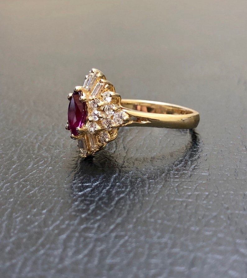 May include: A gold ring featuring a large, oval ruby surrounded by smaller diamonds. The ring is set in a delicate, floral design.