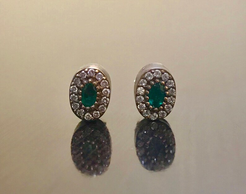 May include: A pair of silver earrings with a green oval gemstone surrounded by small white stones.