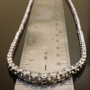 May include: A silver tennis necklace with a row of small, round diamonds. The necklace is laid on a ruler, showing the length to be about 18 inches.
