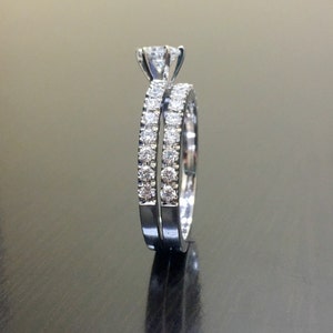 May include: A set of two silver engagement rings with a single large diamond on the top ring and smaller diamonds encircling both rings.