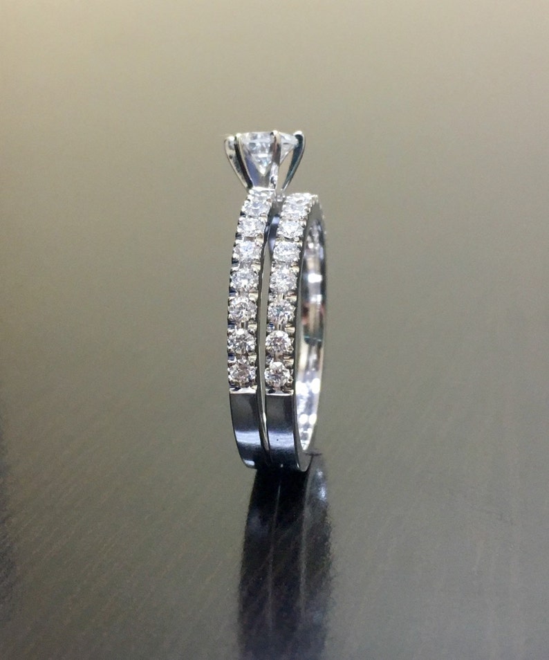 May include: A set of two silver engagement rings with a single large diamond on the top ring and smaller diamonds encircling both rings.