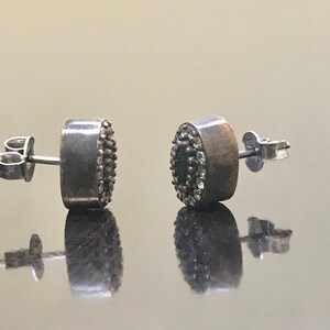 May include: A pair of silver earrings with a round green stone surrounded by small white stones.