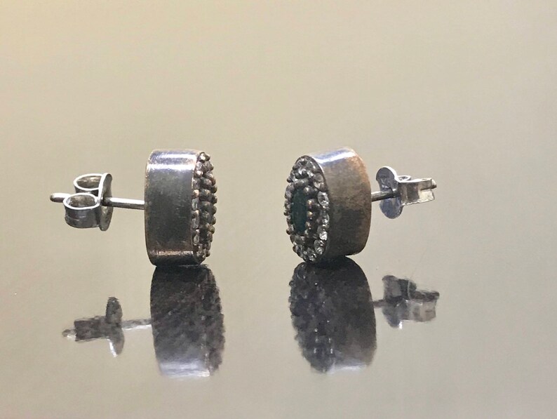 May include: A pair of silver earrings with a round green stone surrounded by small white stones.