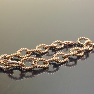 Puede incluir: Un brazalete dorado con un dise&ntilde;o de cadena tipo cuerda. El brazalete est&aacute; hecho de eslabones ovalados.