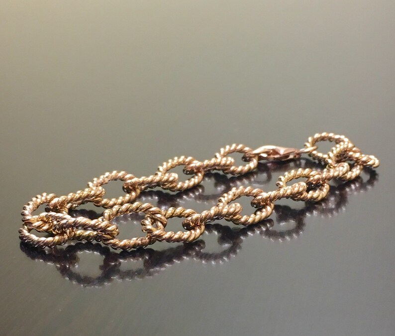 Puede incluir: Un brazalete dorado con un dise&ntilde;o de cadena tipo cuerda. El brazalete est&aacute; hecho de eslabones ovalados.
