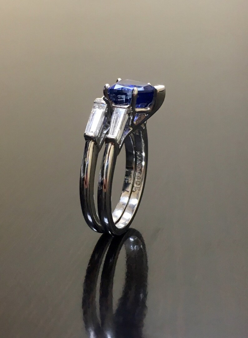 May include: A silver ring set with a blue sapphire and two baguette-cut diamonds. The ring is engraved with the word "MADE".
