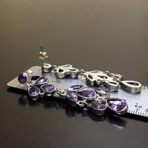 May include: A pair of silver dangle earrings with purple amethyst stones. The earrings are about 2 inches long and feature a delicate floral design.