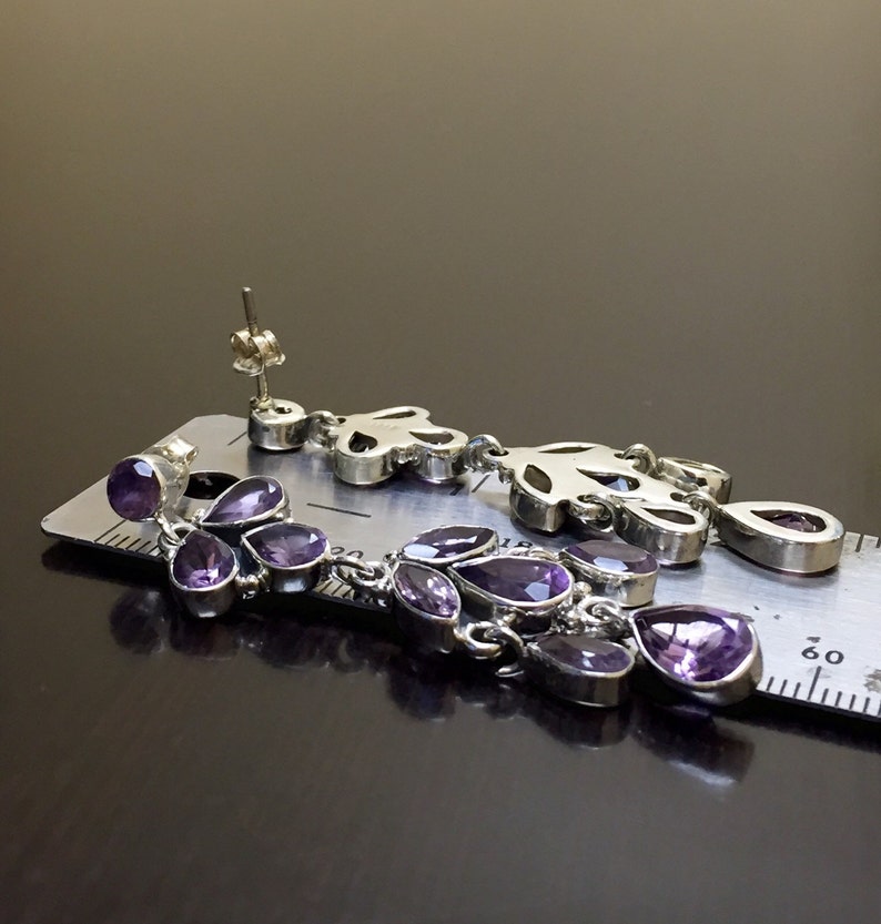 May include: A pair of silver dangle earrings with purple amethyst stones. The earrings are about 2 inches long and feature a delicate floral design.