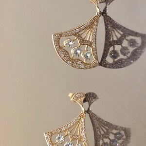May include: A pair of gold earrings with a fan-shaped design and clear stones. The earrings are delicate and intricate.