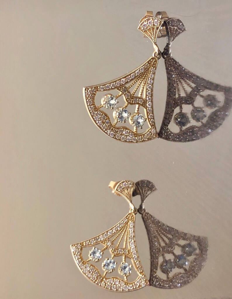 May include: A pair of gold earrings with a fan-shaped design and clear stones. The earrings are delicate and intricate.
