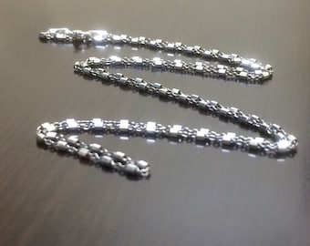 May include: A silver chain necklace with a box chain design. The chain is made of small, square links.
