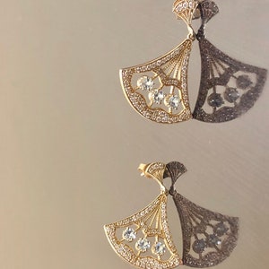 May include: A pair of gold earrings with a fan-shaped design and clear crystal accents.