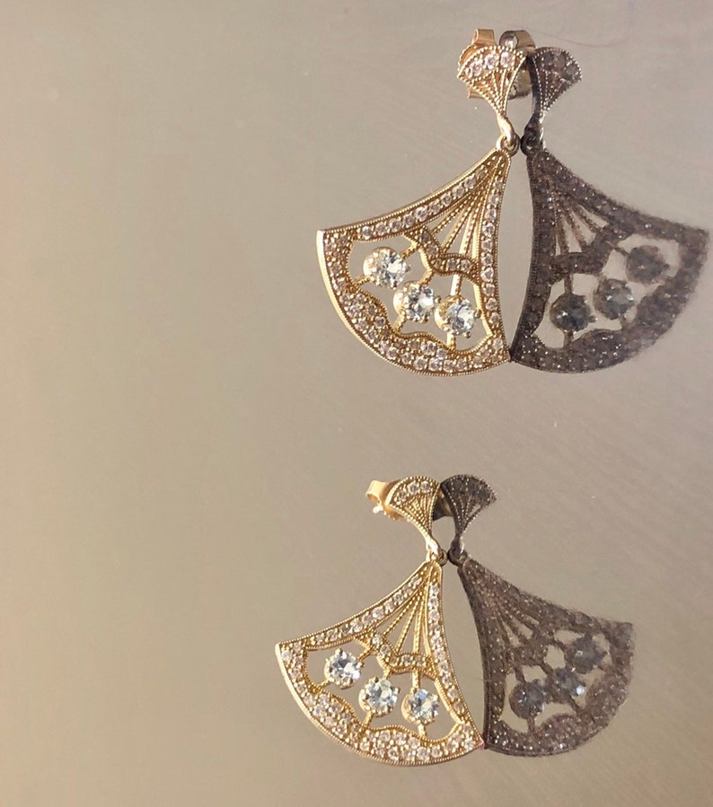 May include: A pair of gold earrings with a fan-shaped design and clear crystal accents.