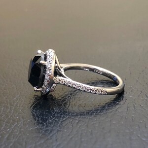 May include: A silver ring with a large black gemstone surrounded by a halo of smaller diamonds. The band is also set with diamonds.