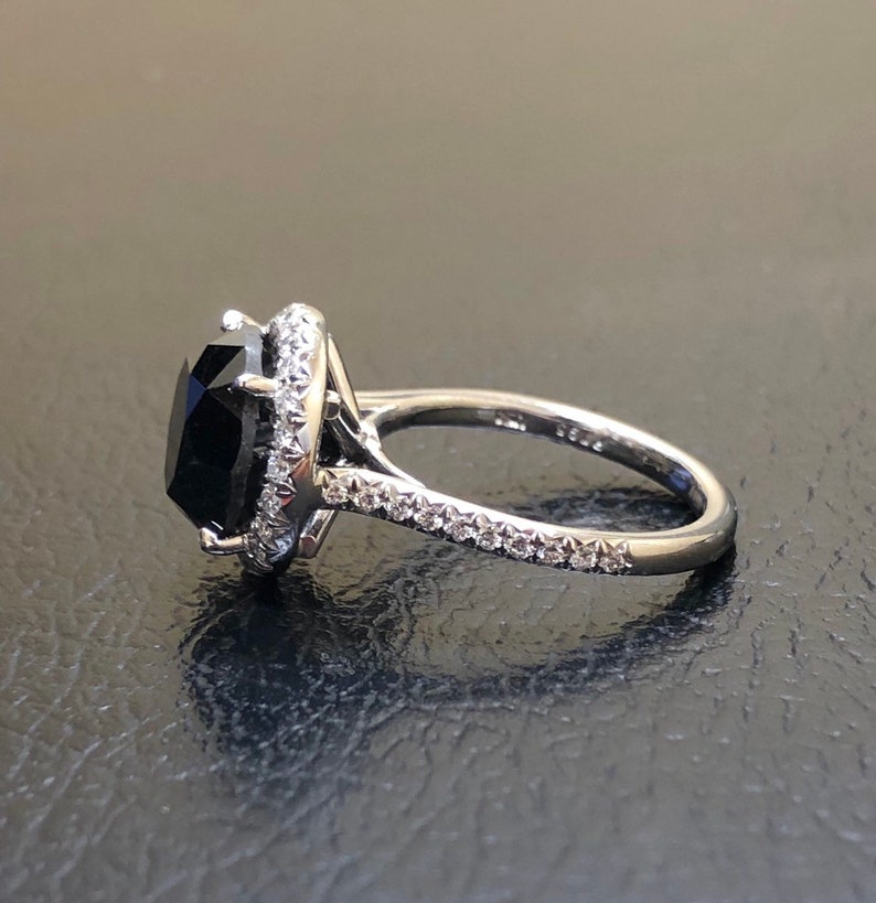 May include: A silver ring with a large black gemstone surrounded by a halo of smaller diamonds. The band is also set with diamonds.