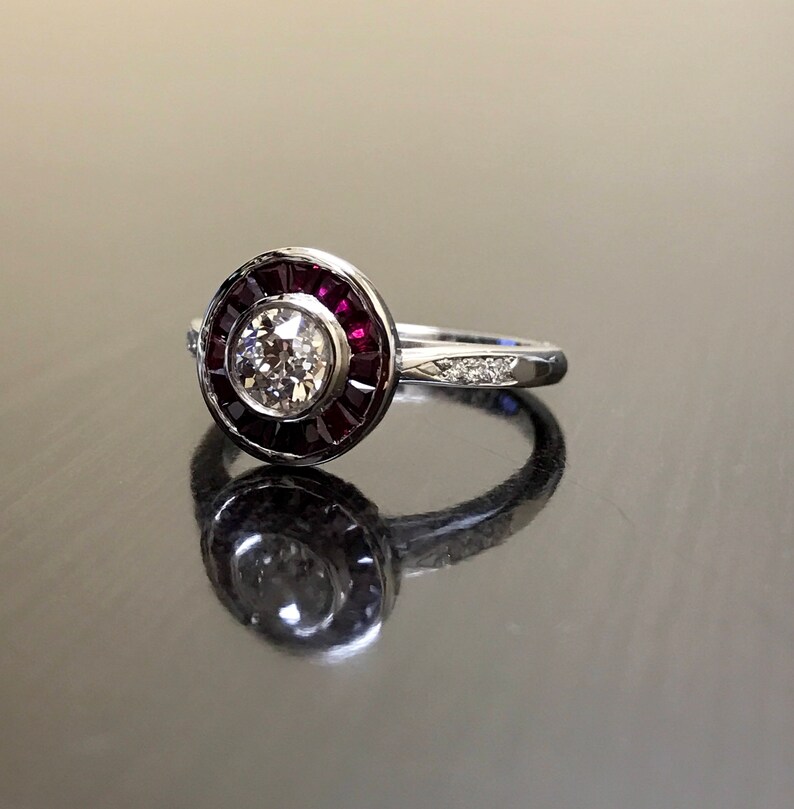 May include: A silver ring with a round center stone surrounded by a halo of red rubies. The band is set with smaller diamonds.