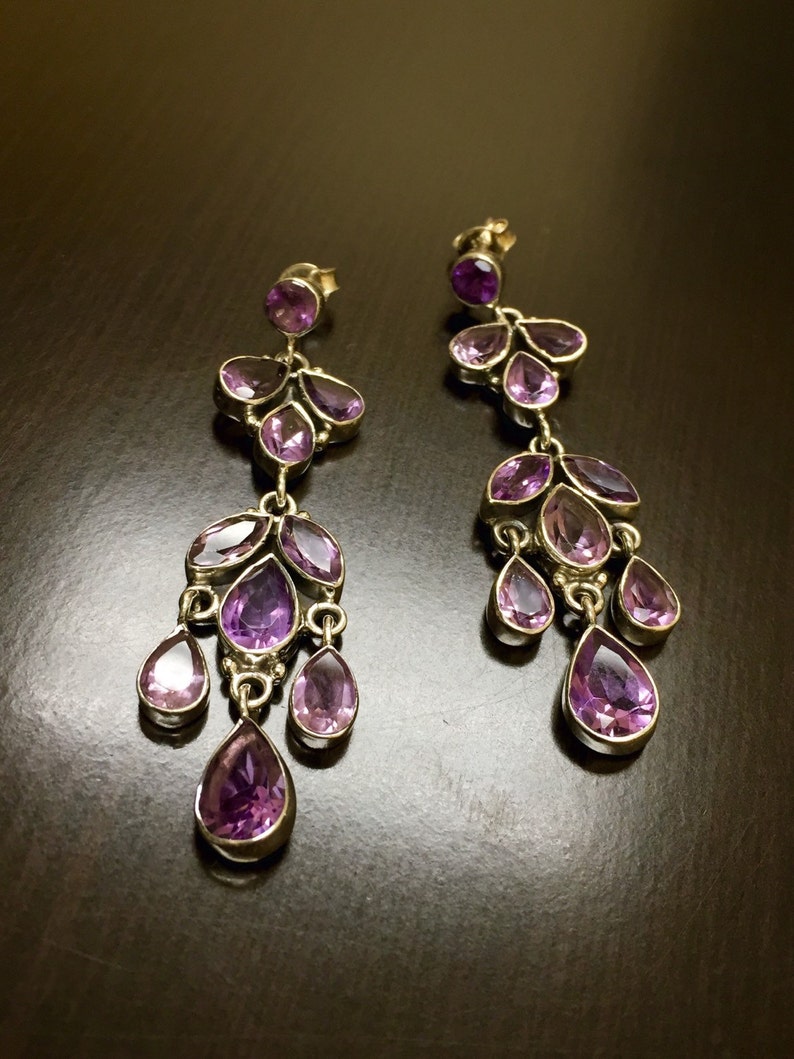 May include: A pair of dangle earrings with multiple purple amethyst stones. The earrings are silver and have a teardrop shape.