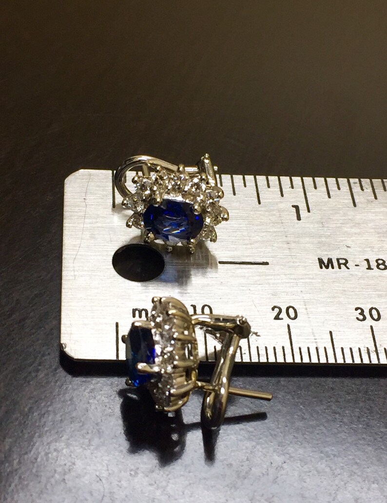May include: A pair of silver earrings with a blue gemstone surrounded by smaller clear gemstones. The earrings have a clip-on closure.