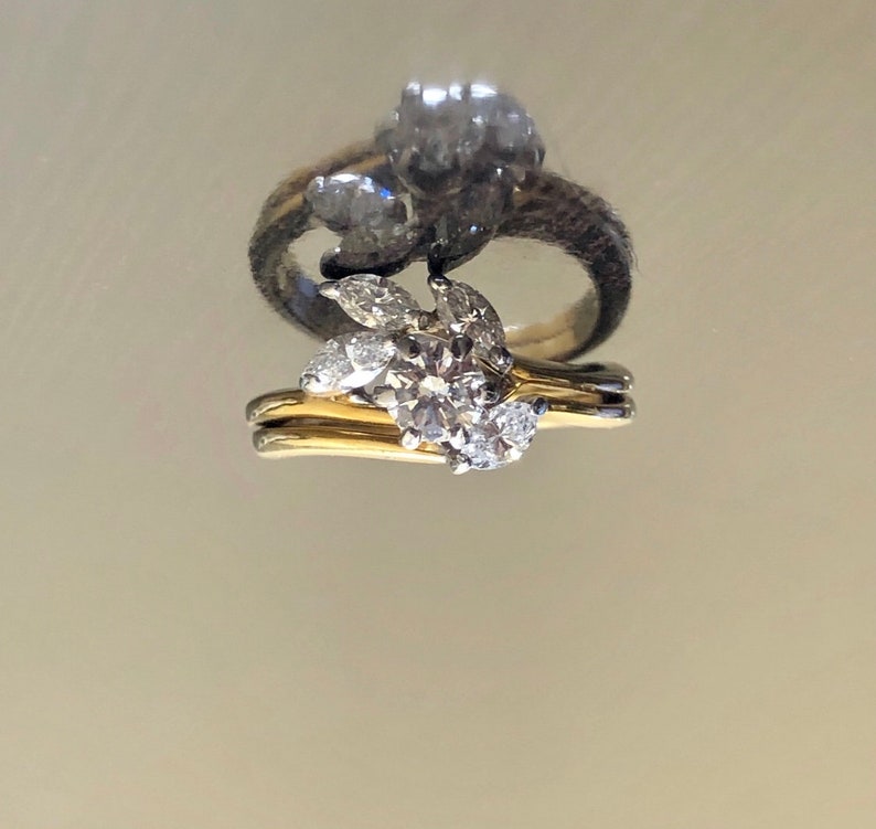 May include: A pair of gold and silver engagement rings with a large round diamond and smaller diamonds set in a leaf design.