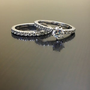 May include: A set of two silver wedding bands with a single round diamond on the top band. Both bands are set with small diamonds.