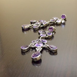 May include: A pair of dangle earrings with multiple purple amethyst stones and silver settings.