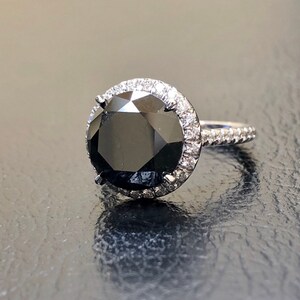 May include: A black diamond engagement ring with a halo of smaller diamonds set in white gold.