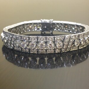 Puede incluir: Un brazalete de plata con una fila de diamantes redondos engastados en un dise&ntilde;o delicado e intrincado. El brazalete est&aacute; hecho de metal y tiene un acabado pulido.
