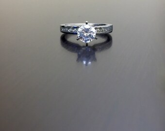 May include: A silver engagement ring with a single round diamond and a band of smaller diamonds.