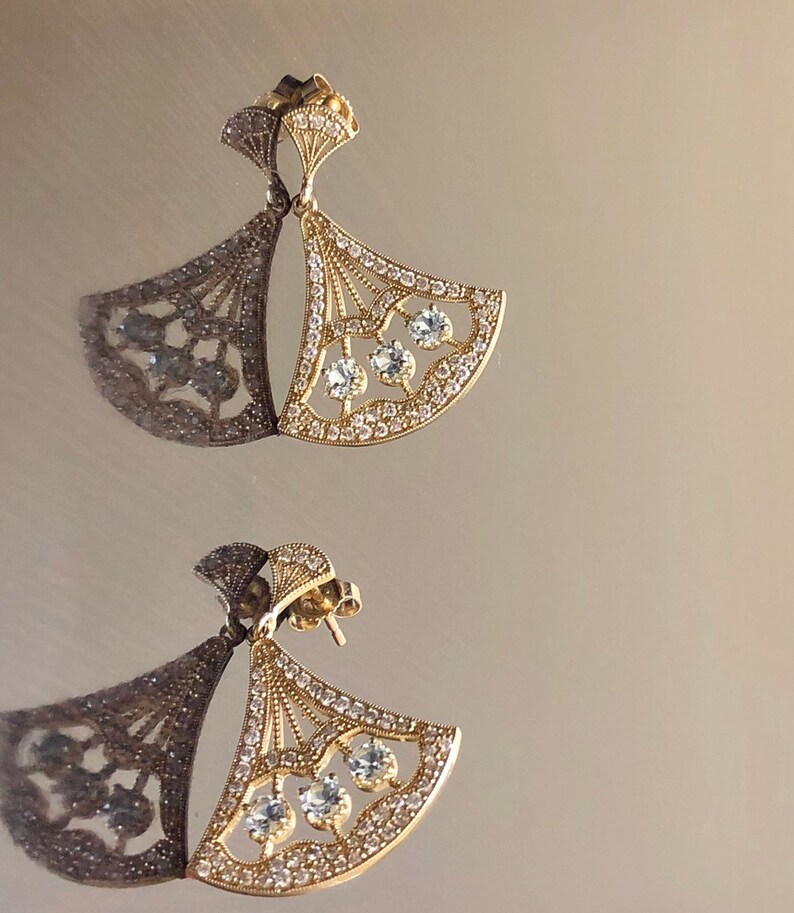 May include: A pair of gold earrings with a fan-shaped design and clear crystals. The earrings are delicate and elegant.