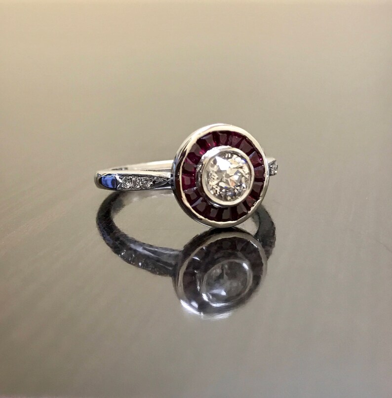 May include: A silver ring with a round center stone surrounded by a halo of red rubies. The band is set with smaller diamonds.