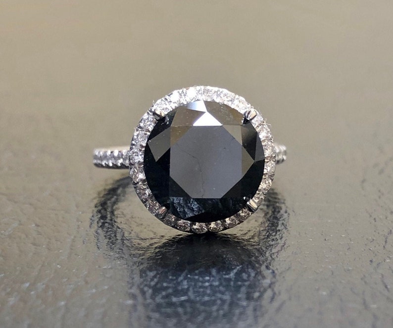 May include: A black diamond engagement ring with a halo of smaller diamonds set in white gold.